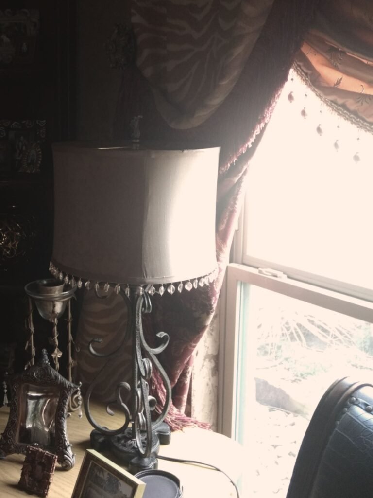 Taupe drum-style lampshade atop outdated wrought iron lamp base